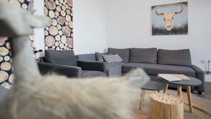 Ein modernes Wohnzimmer mit einem grauen Sofa, einem runden Holztisch und einer Wand mit Holzmuster.