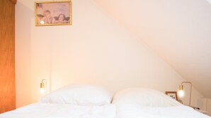 Ein ordentlich bezogenes Bett mit weißer Bettwäsche in einem Zimmer mit schrägem Dach.
