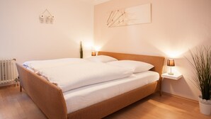 A bedroom with a wooden bed, white bedding, two bedside tables with lamps, a radiator, and a wall-mounted artwork. - Large Apartment near Ski Area in Winterberg Germany (Winterberg)