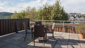A terrace with wicker furniture and a view of a town and hills. - Large Apartment near Ski Area in Winterberg Germany (Winterberg)