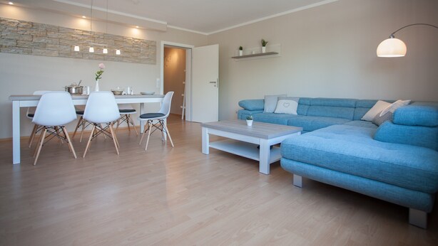A modern living room with a blue sofa, white dining chairs, a wooden coffee table, and a stone wall. - Large Apartment near Ski Area in Winterberg Germany (Winterberg)