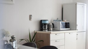 A modern kitchen with a microwave, coffee maker, and a refrigerator. There is a small table with chairs and a potted plant. - Scenic Apartment in Maslenica With Terrace (Jasenice)
