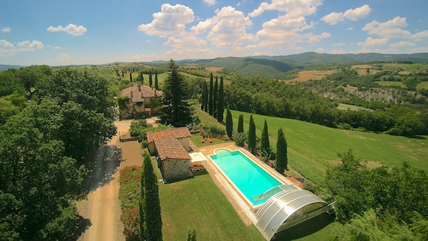 A large swimming pool with a glass enclosure, surrounded by lush greenery and a hilly landscape. - Elysian Escape - A Paradise (San Venanzo)