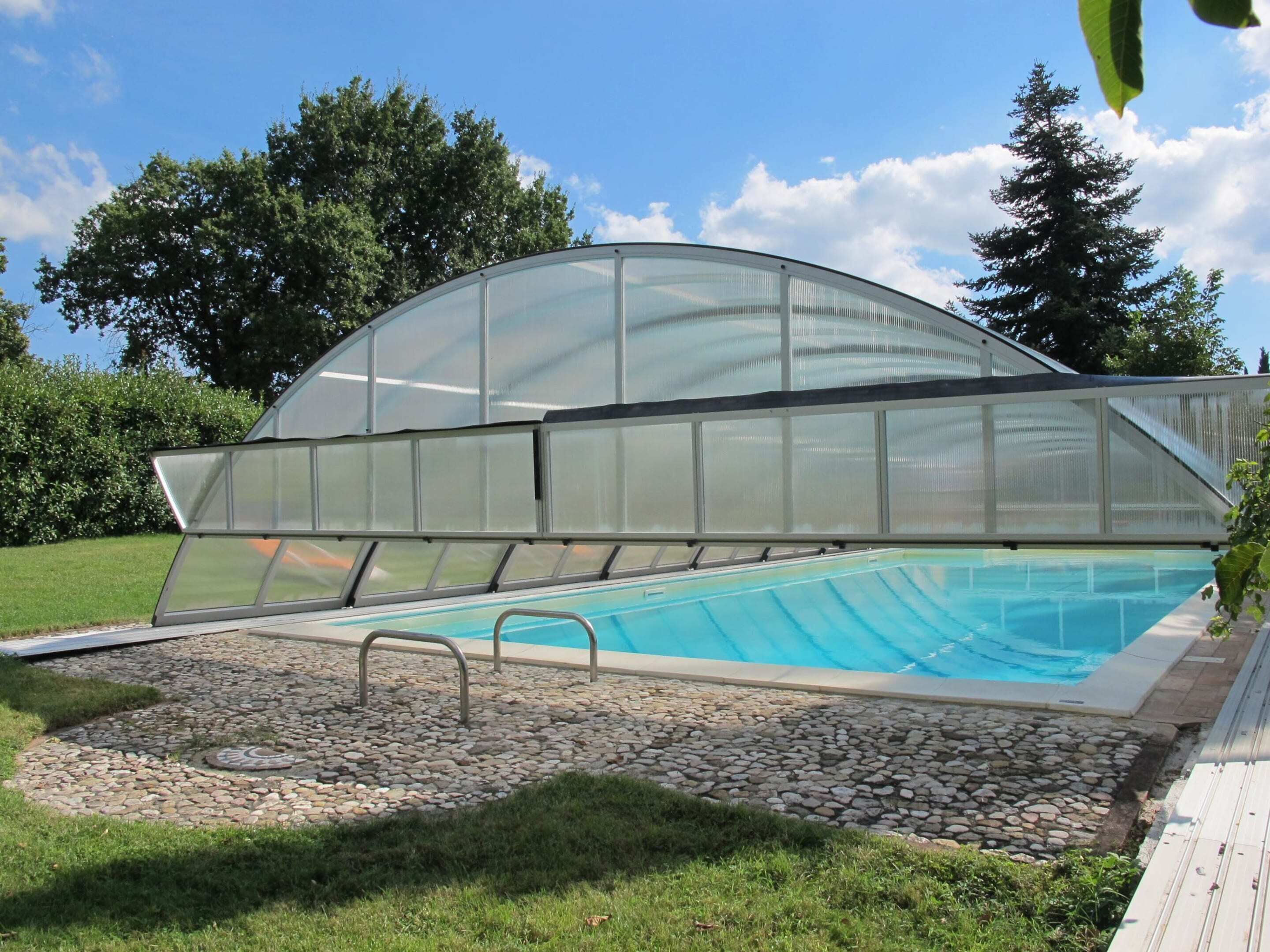 A swimming pool with a glass-enclosed area, surrounded by a stone pathway and greenery.