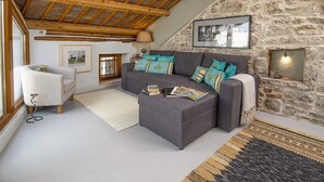 A cozy living room with a stone wall, a grey sofa with colorful cushions, a white armchair, and a wooden ceiling. - Holiday Home in Vodnjan Near the Sea (Vodnjan)