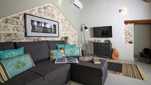 A living room with a stone wall, a grey sofa, a flat-screen TV, and a bookshelf. - Holiday Home in Vodnjan Near the Sea (Vodnjan)