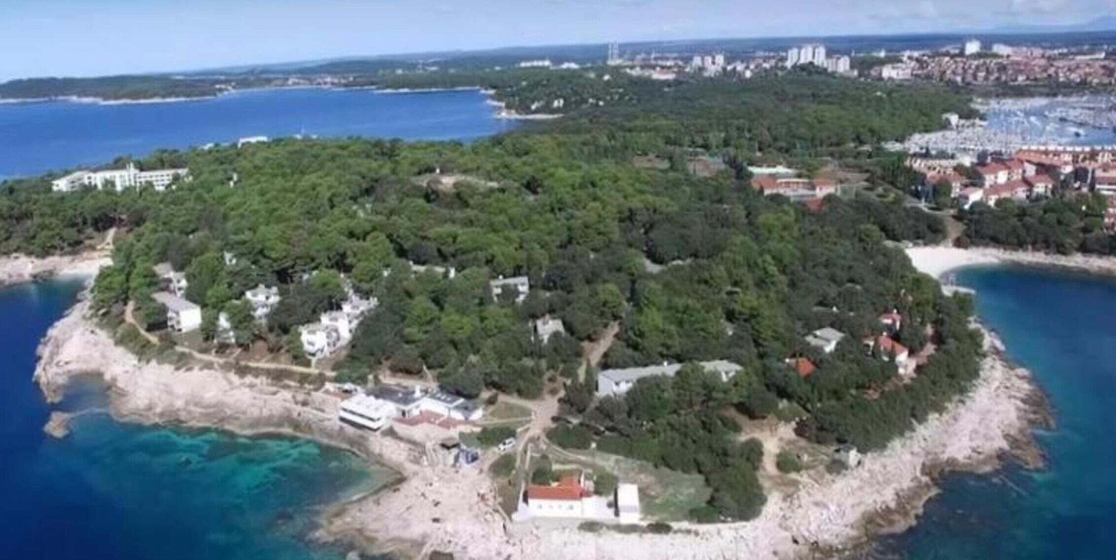 An aerial view of a coastal island with buildings, clear blue waters, and a beach.