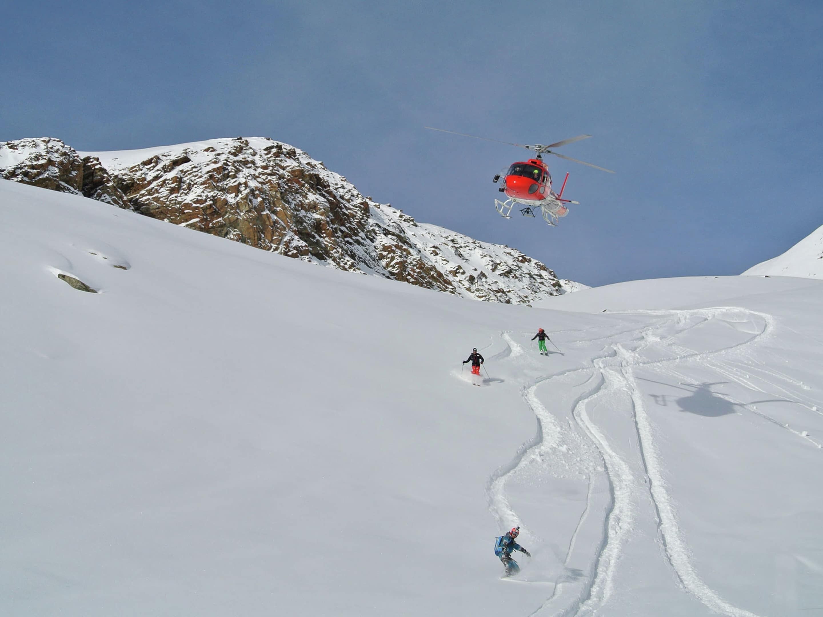 A helicopter flying over a snowy mountain with skiers on a slope.