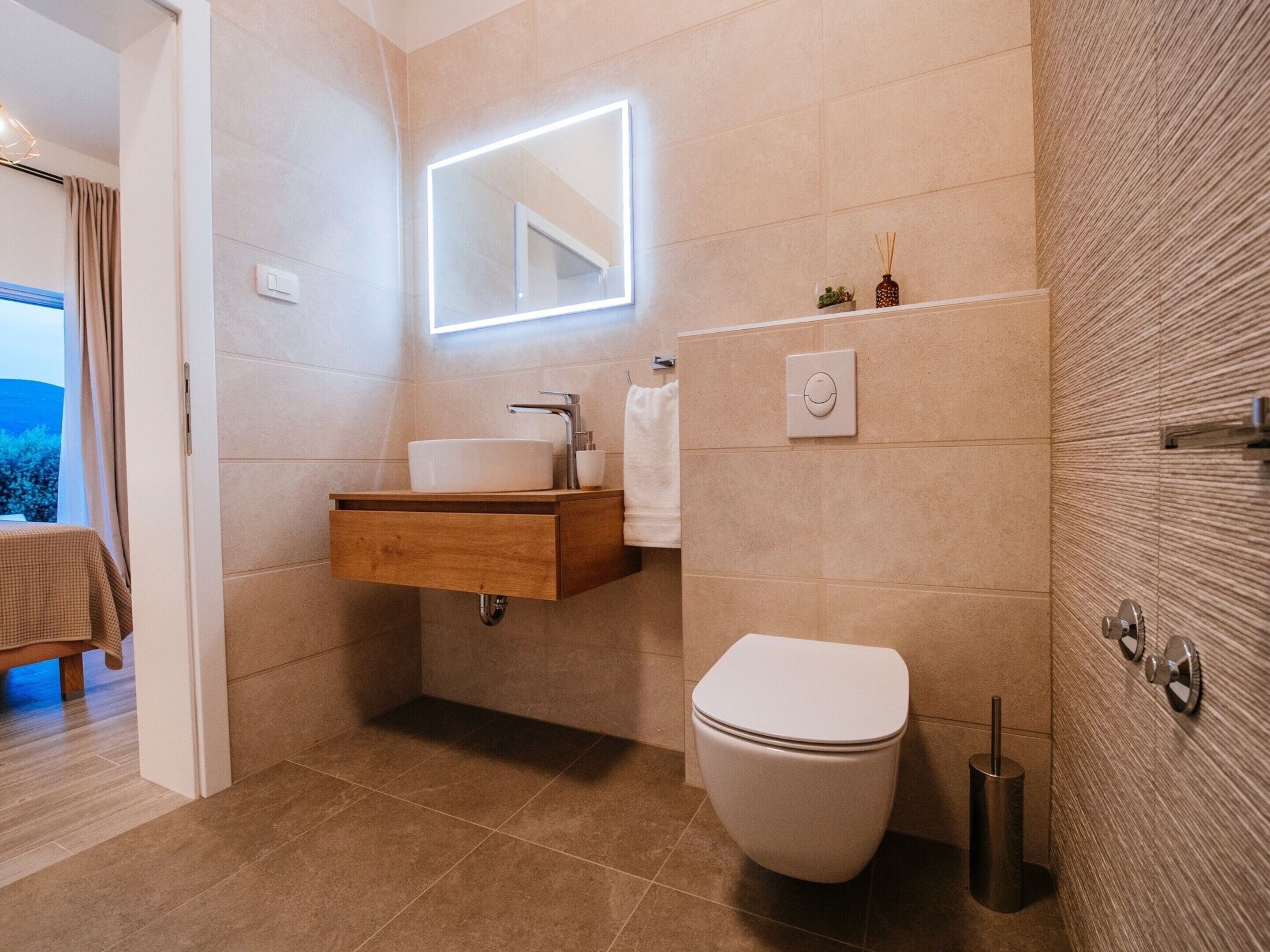 A modern bathroom with a built-in sink, a toilet, and a mirror with integrated lighting.