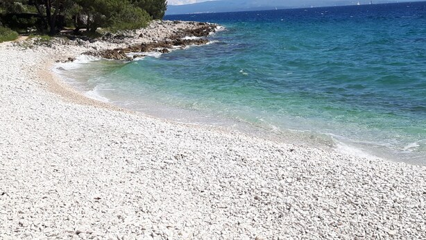 Ein Kiesstrand mit klarem Wasser und einer felsigen Küste.