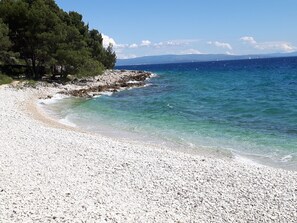 A pebble beach with clear water and a rocky shoreline. - Nice Apartment With Shared Swimming Pool Near the Beach and Trogir (Okrug)
