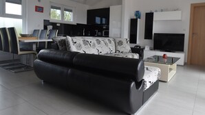 Ein modernes Wohnzimmer mit einer schwarzen Ledersofa, einer Essecke mit Tisch und Stühlen, einer Küche und einem großen Fenster.