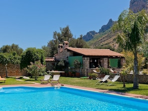 Eine Steinvilla mit Swimmingpool, grünen Fensterläden und einem Bergpanorama.