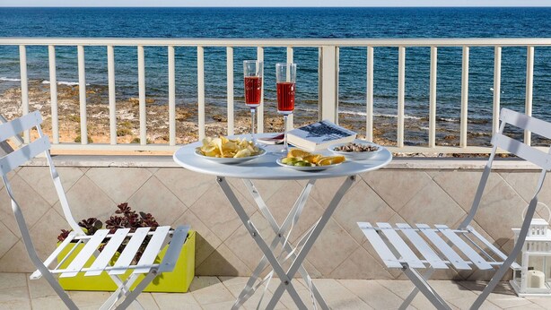 Une table dressée avec de la nourriture et des boissons sur un balcon donnant sur la mer.