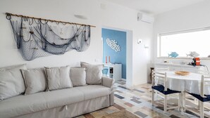 Un salon avec un canapé, un coin repas avec une table et des chaises, un espace cuisine et un mur d’accent bleu.