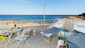 Un balcon avec vue sur la mer, des meubles blancs et une table garnie de nourriture.