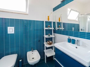 Features a sleek design with a bidet, toilet, and large mirror.