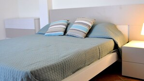A bed with a quilted blue bedspread and two striped pillows, a bedside table with a lamp, and a white headboard. - Holiday Home in Lazise Near Lake Garda (Lazise)