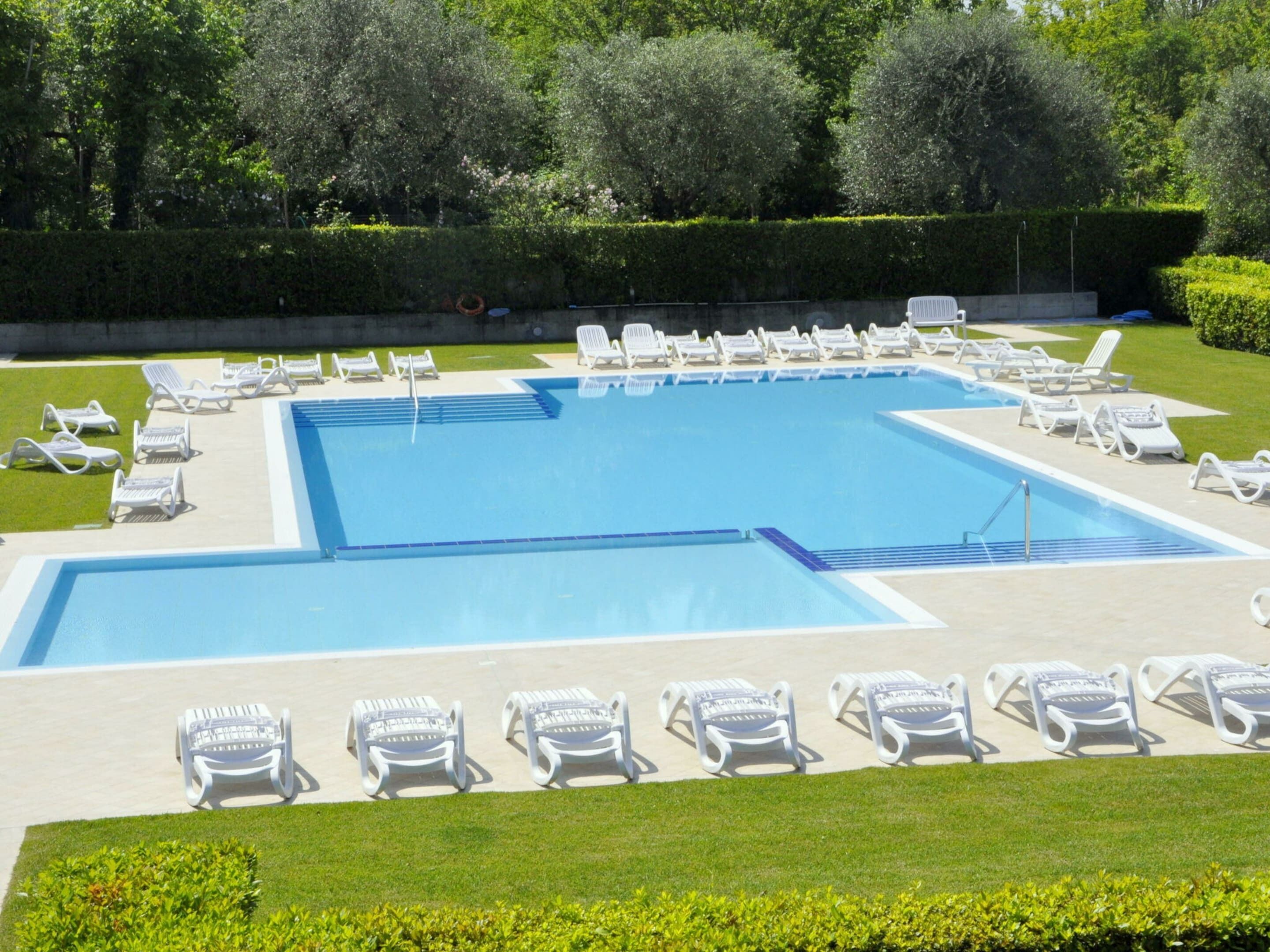 A rectangular swimming pool with multiple lanes, surrounded by white lounge chairs and a well-maintained lawn.