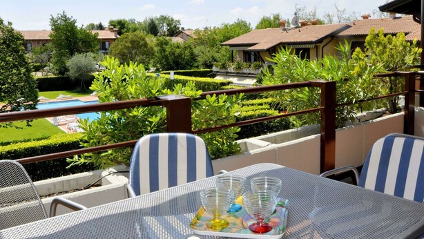 An outdoor seating area with a pool view, featuring a table with chairs and a glass tray with glasses and a bottle. - Holiday Home in Lazise Near Lake Garda (Lazise)