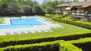 A large rectangular swimming pool with multiple white lounge chairs arranged around it. - Holiday Home in Lazise Near Lake Garda (Lazise)