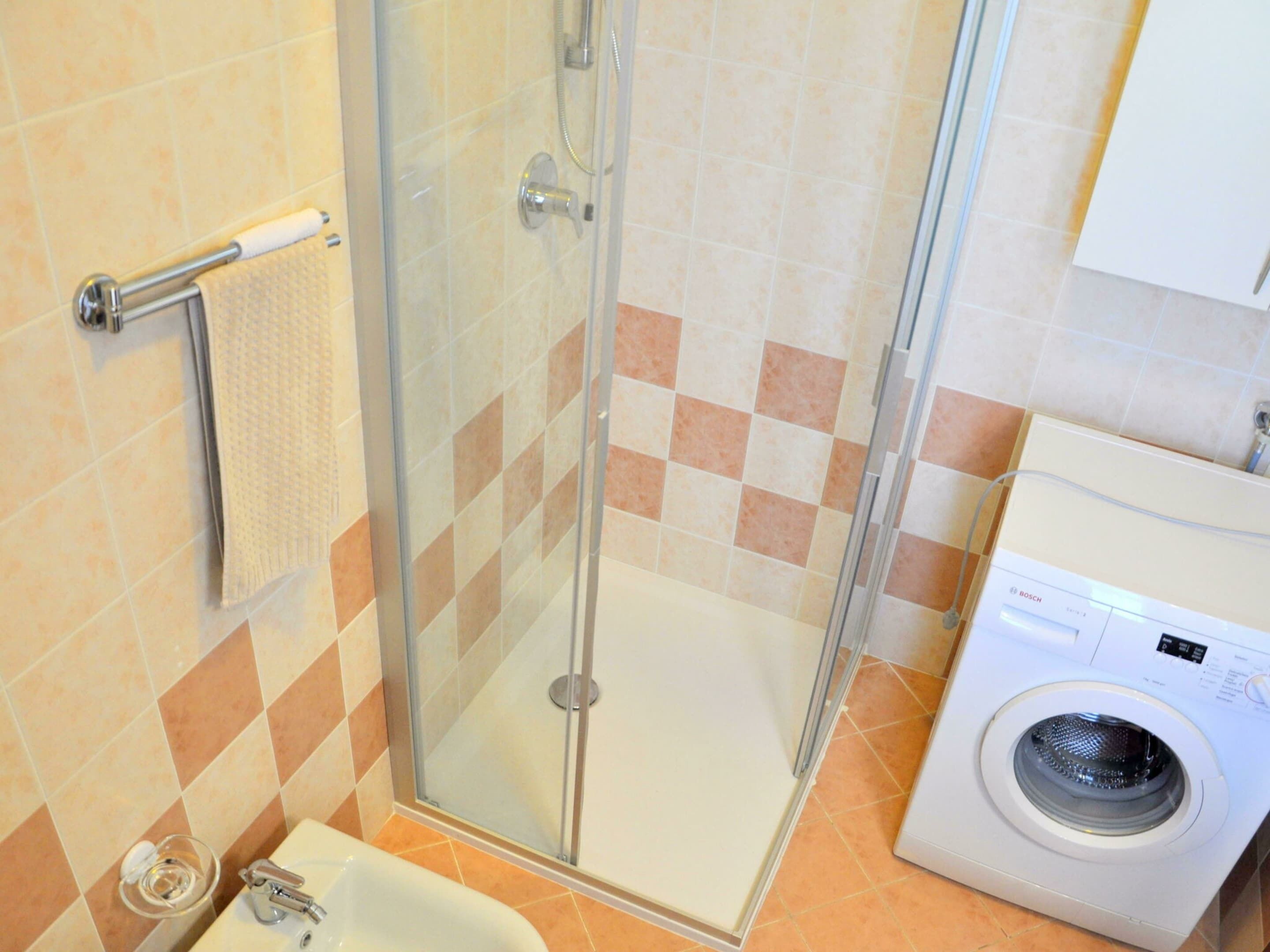 Une salle de bain avec une douche à parois de verre, des toilettes, un lavabo et un lave-linge.
