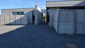 A modern building with a concrete exterior, large windows, and a gravel driveway. - Modern Dalhem Villa With Views (Dalhem)