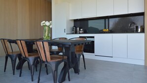 A modern kitchen with white cabinets, a black countertop, and a dining area with a table and chairs. - Modern Dalhem Villa With Views (Dalhem)