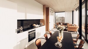 A modern kitchen with white cabinetry, a black countertop, and a dining area with a dark wooden table and chairs. - Modern Dalhem Villa With Views (Dalhem)