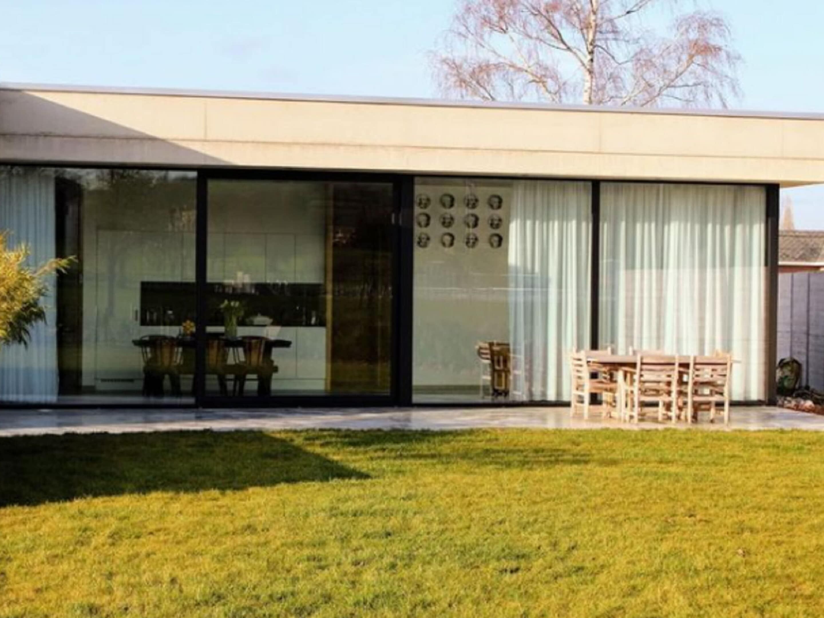 A modern house with a large glass door leading to a dining area.