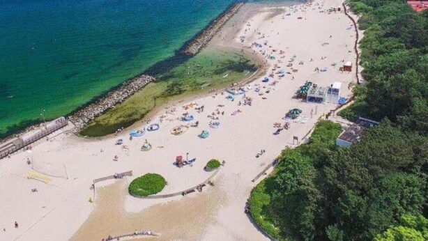 An aerial view of a beach with clear waters, a sandy shore, and several beach umbrellas and sun loungers. - Apartment in Dar?owo With Garden (Darlowo)