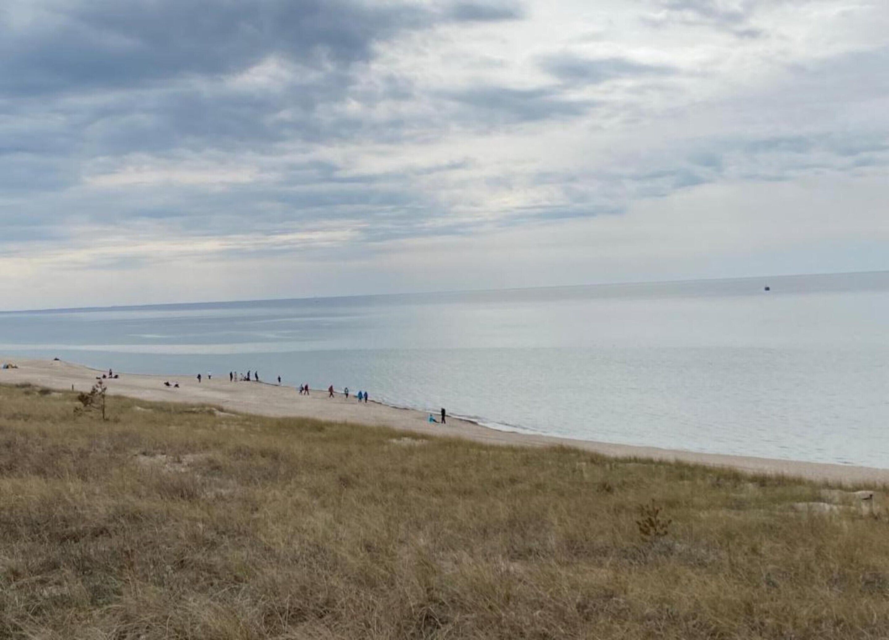 Una playa con gente caminando por la orilla, cielo despejado y mar tranquilo.