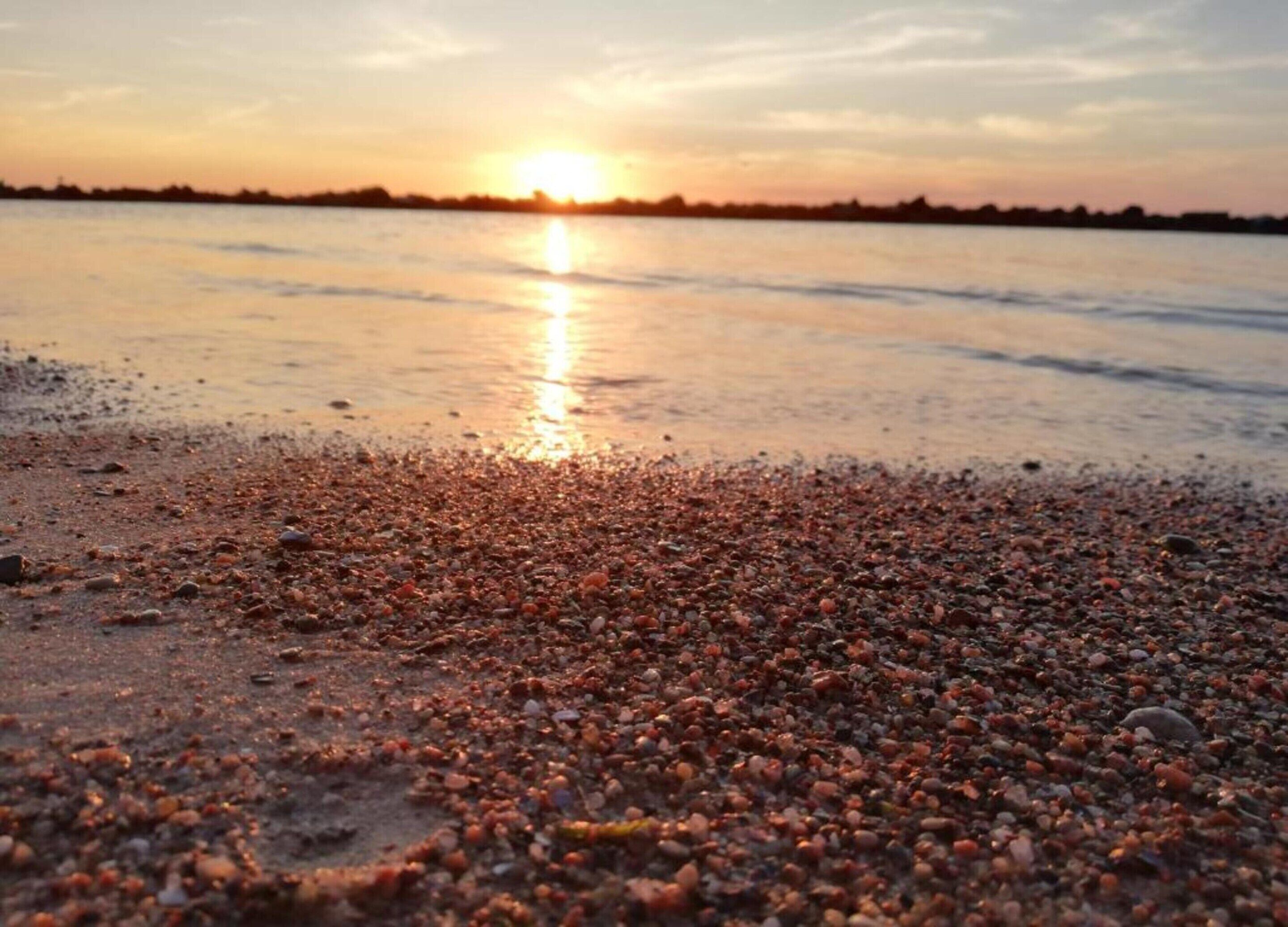 A beach with pebbles and a sunset in the background.