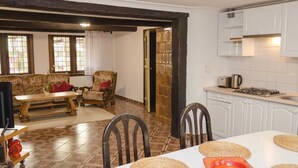 A cozy living room with a sofa, armchair, and a dining table with placemats. A kitchen with white cabinets and a gas stove is visible. - Apartment in Dar?owo With Garden (Darlowo)