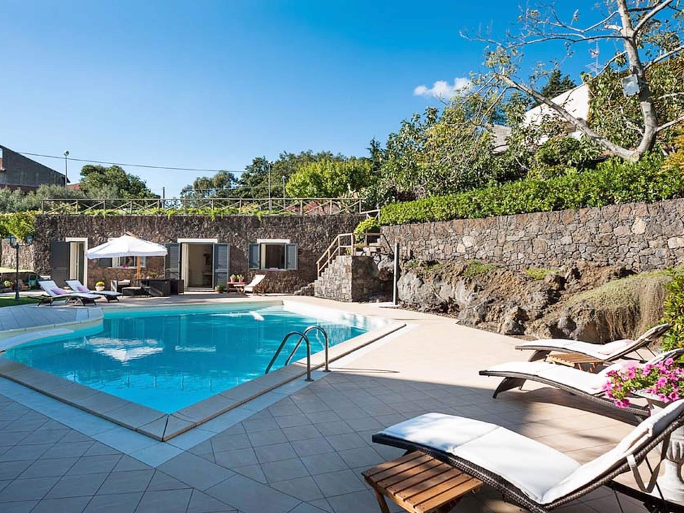 A swimming pool with lounge chairs and a stone wall.