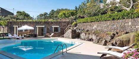 Una piscina con sillones de descanso y un muro de piedra.