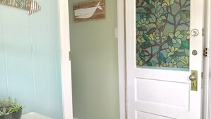 Un pasillo con una puerta blanca que tiene un vitral, un estante pequeño con una planta y un cartel fijado a la pared.