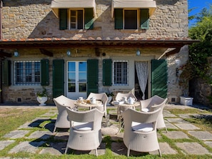 A stone building with green shutters, a terrace with wicker furniture, and a view of the countryside. - Belvilla by OYO Femar REQ (Cortona)