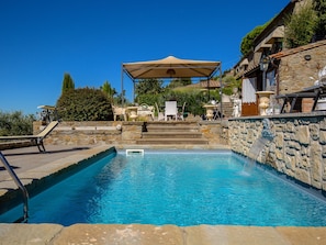 A swimming pool with a stone wall and a pergola with a canopy. - Belvilla by OYO Femar REQ (Cortona)