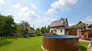 A backyard with a wooden swimming pool, a swing set, and a house. - Holiday Home With Private Pool in Bohemian (Vrchlabi)