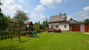A residential property with a well-maintained lawn, a wooden play structure, a house with a garage, and a clear sky. - Holiday Home With Private Pool in Bohemian (Vrchlabi)