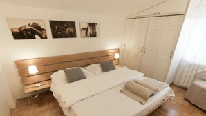 Une chambre à coucher avec un lit en bois, du linge de lit blanc, une table de chevet avec une lampe et une armoire.