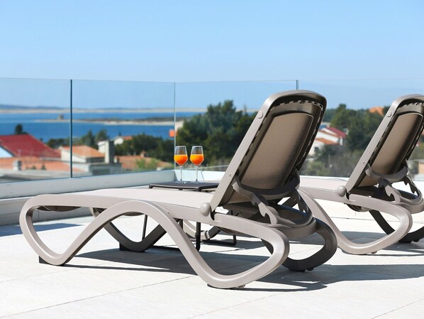 Deux fauteuils confortables avec une table en verre, deux verres de jus d’orange et une vue panoramique sur la mer et les bâtiments.