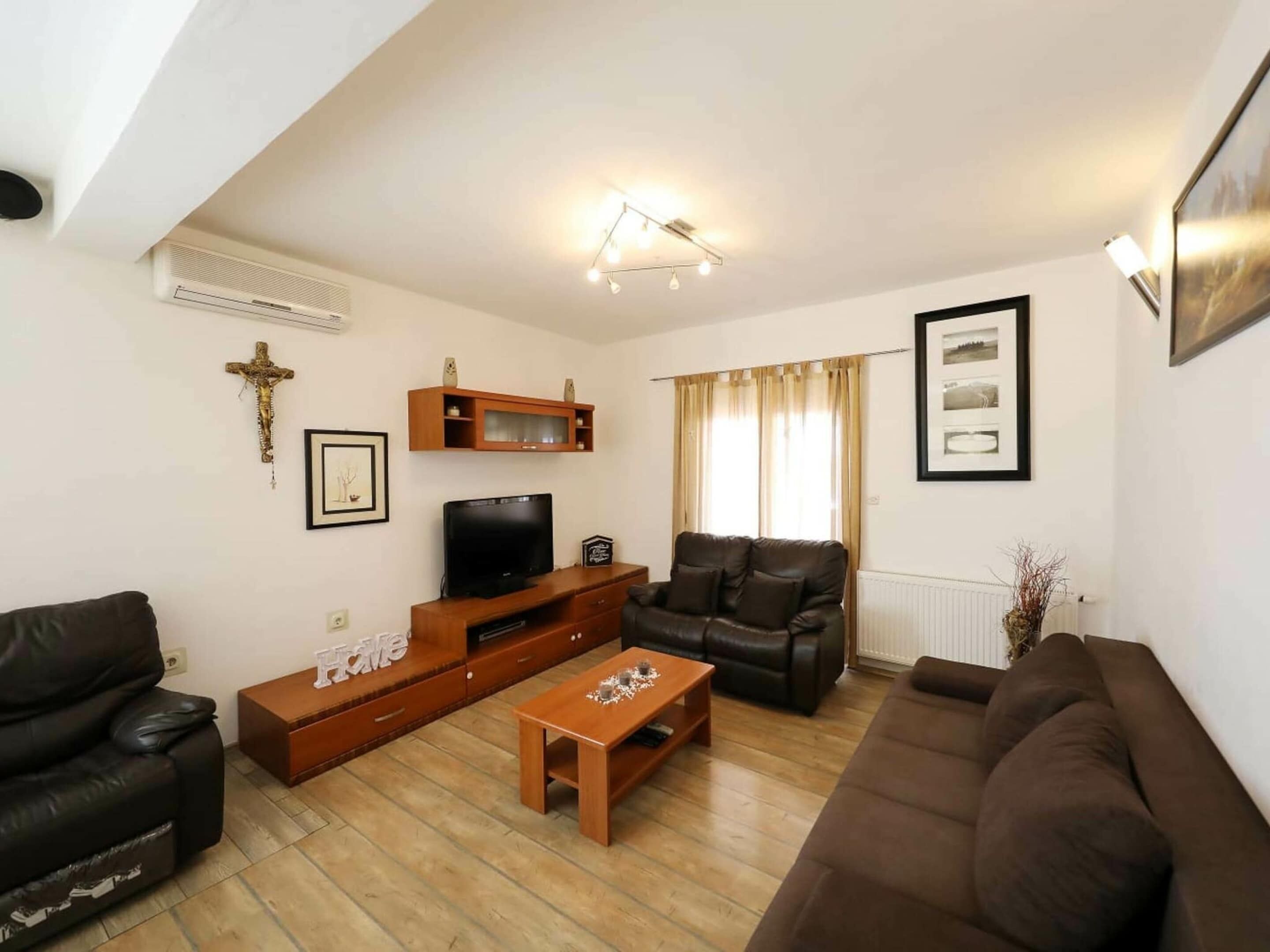 Una sala de estar con televisor, sofás de cuero, una mesa de centro de madera y una cruz en la pared.