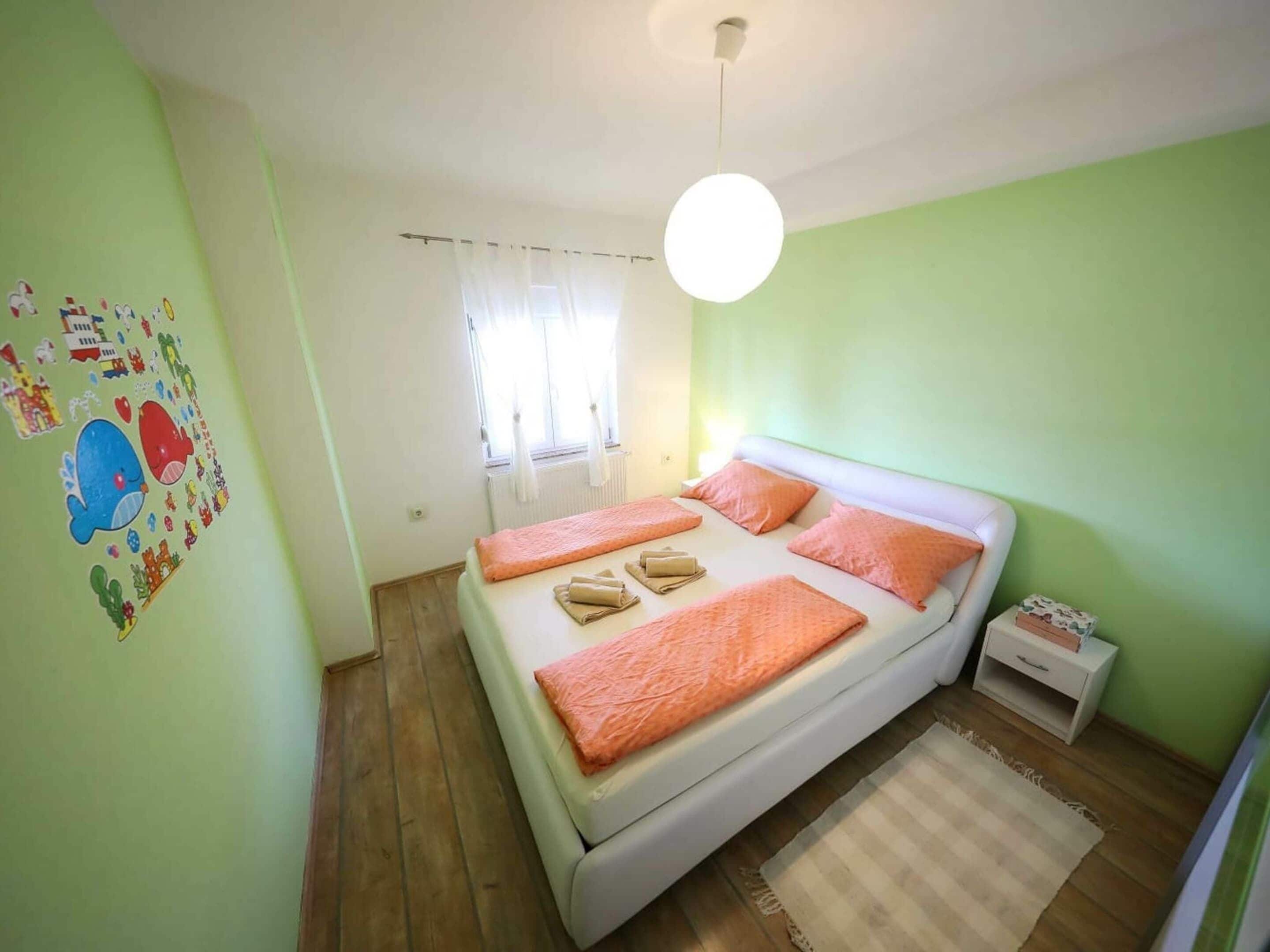 A bedroom with a bed, a bedside table, a nightstand, a window with curtains, and a wall with stickers.