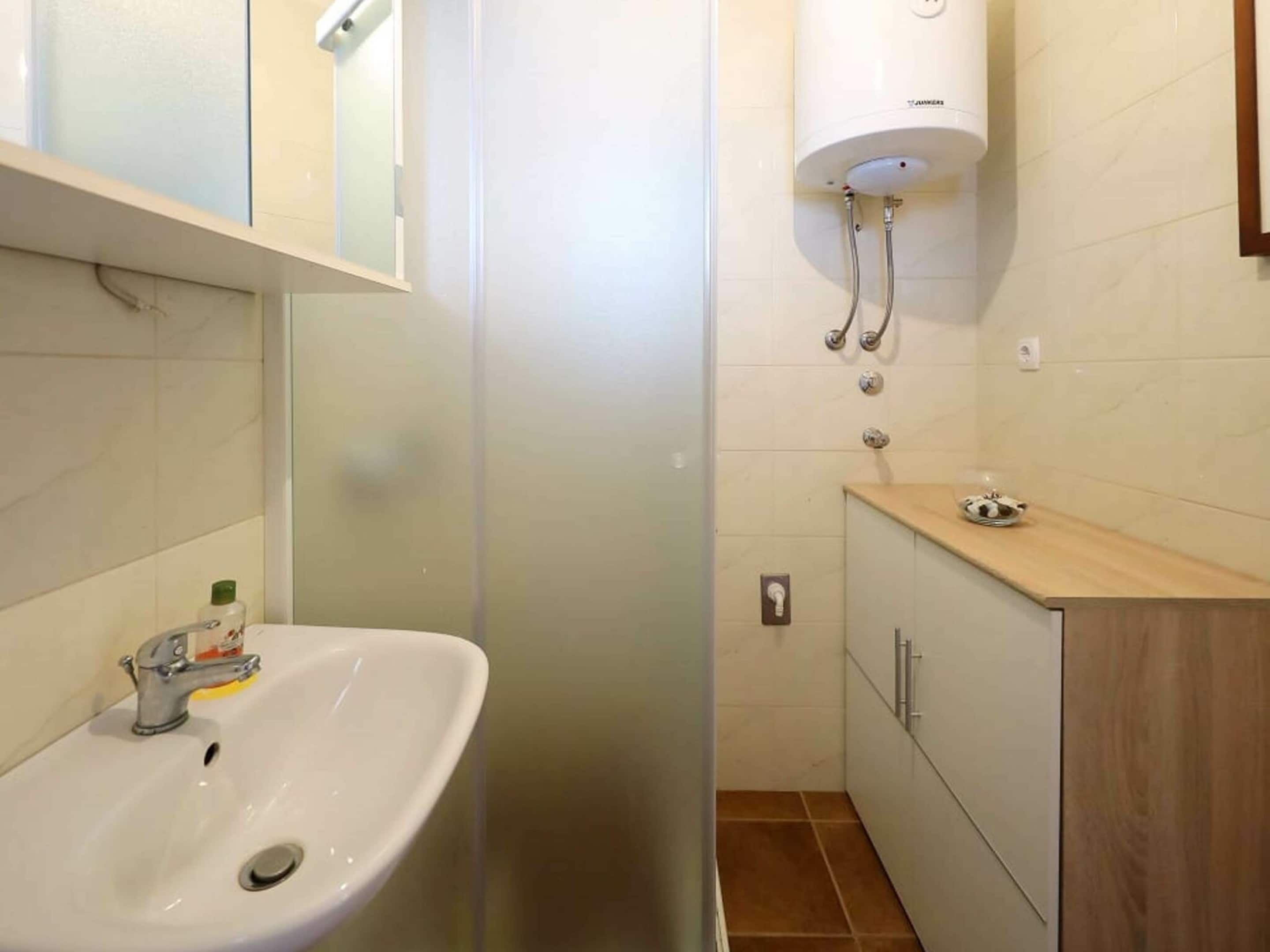 A bathroom with a white sink, a mirror above it, a toilet, and a shower area with a white water heater.