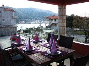 A dining area with tables set for four, outdoor seating, and a view of a town and mountains in the background. - Exquisite Villa with Private Hot Tub in Grebaštica (Sibenik)