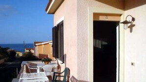 Ein Balkon mit Gartenmöbeln, eine Tür mit einer Nummer und Blick auf das Meer.