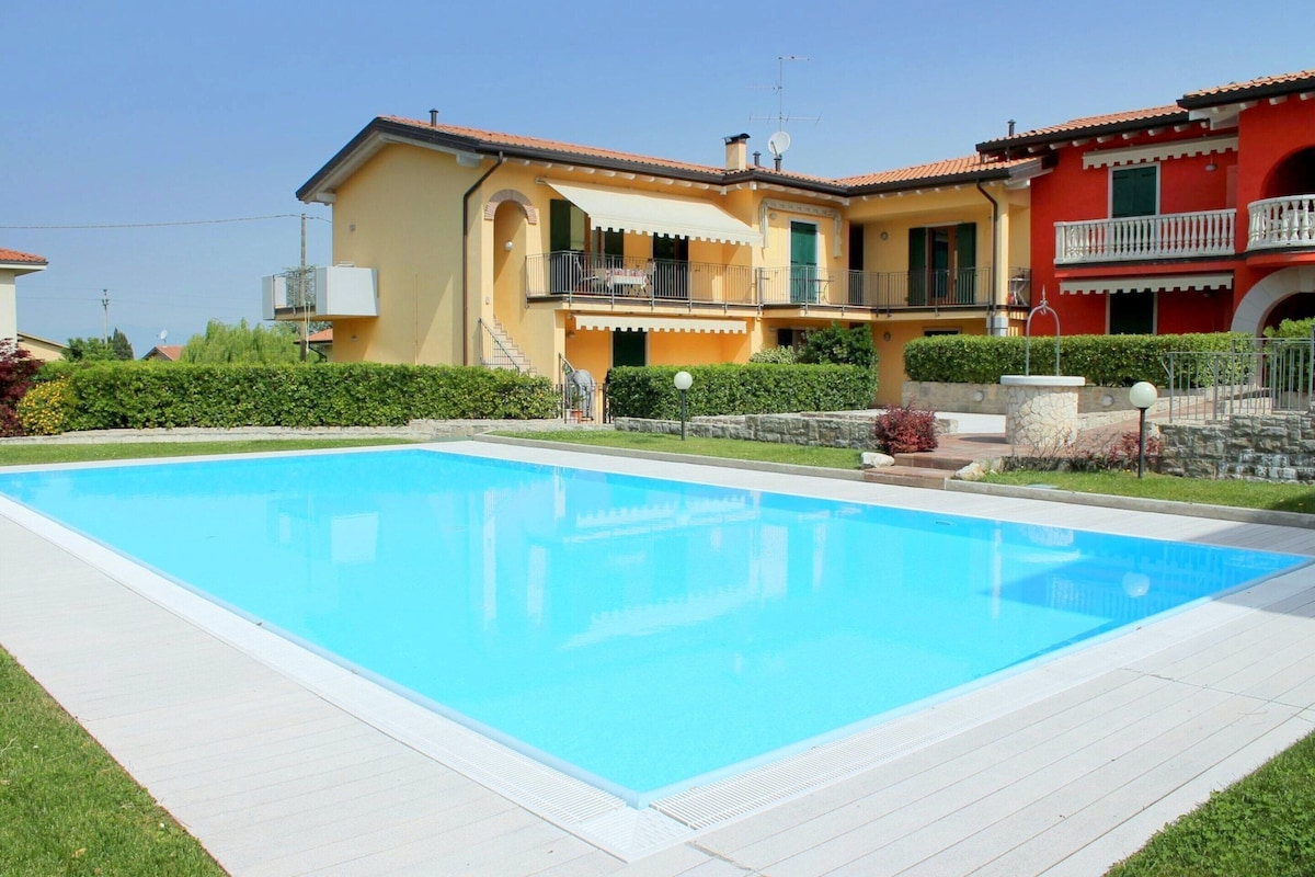 A large rectangular swimming pool with a white deck, surrounded by a well-maintained lawn and a stone wall.