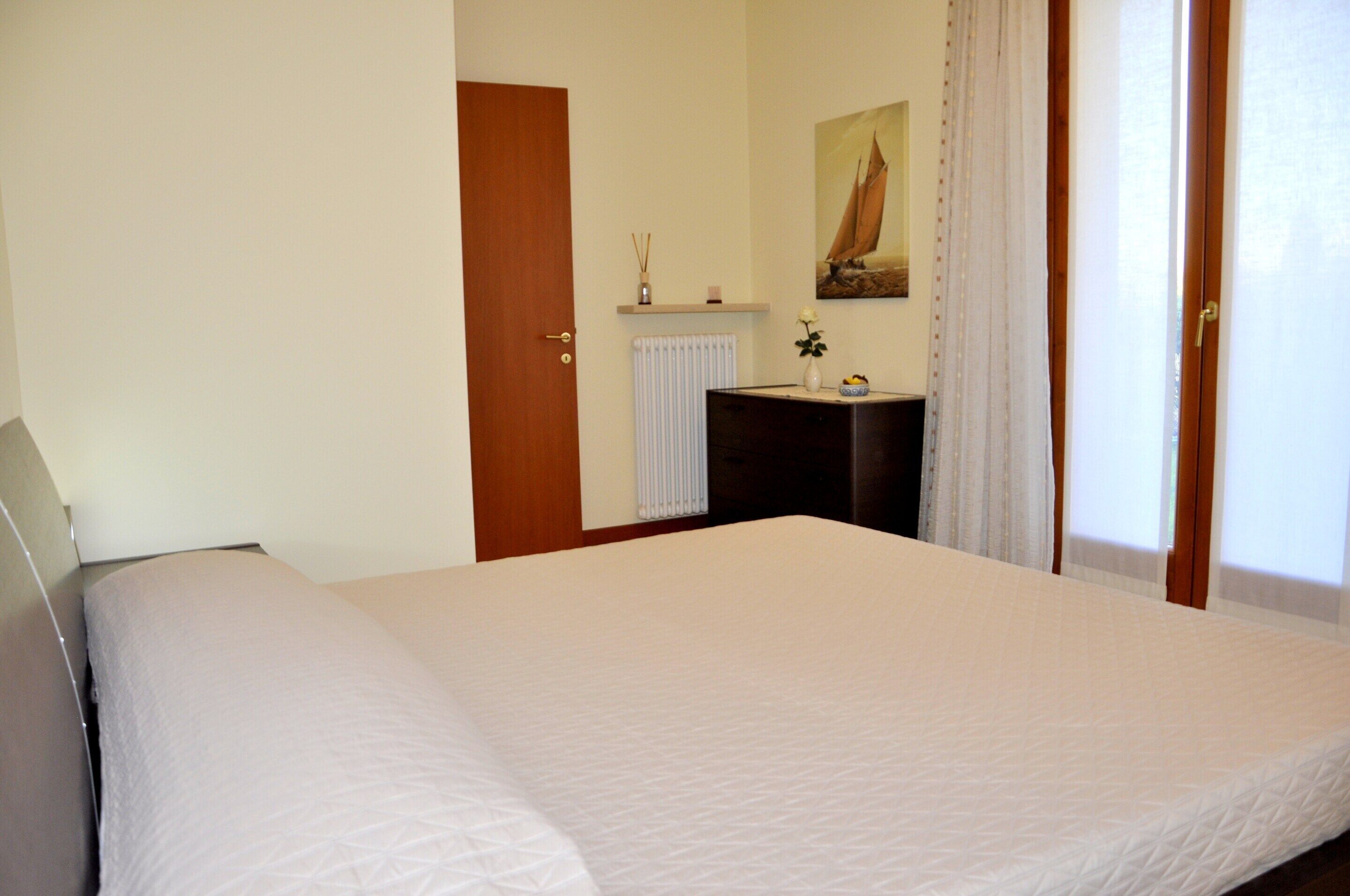 Een slaapkamer met een bed, een dressoir, een radiator, een schilderij en een deur.